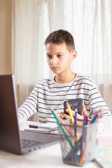 Kid sitting with laptop computer and scrolling phone instead of doing homework at home