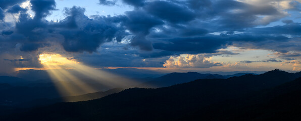 The bright rays of the sun are shining from saturated clouds to mountain range before sunset.