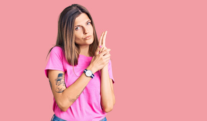 Beautiful caucasian woman wearing casual clothes holding symbolic gun with hand gesture, playing killing shooting weapons, angry face
