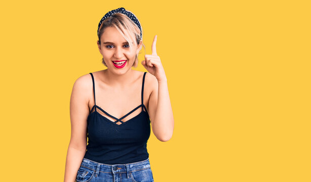 Young beautiful blonde woman wearing casual clothes pointing finger up with successful idea. exited and happy. number one.