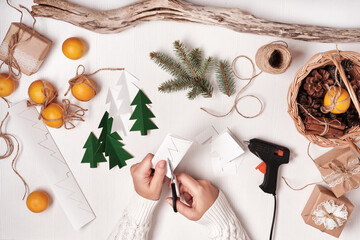 DIY Christmas home decor from natural materials. Hands make garland of paper trees, twine and cones
