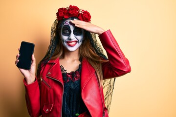 Woman wearing day of the dead costume holding smartphone showing screen stressed and frustrated with hand on head, surprised and angry face