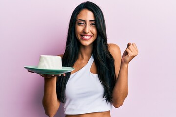 Beautiful hispanic woman eating fresh white cheese screaming proud, celebrating victory and success very excited with raised arm