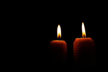 Close-up of two lit yellow candles on a black background.