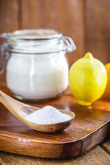 Glass pot with baking soda and wooden measuring spoon, with fruits in the background, lemon and orange, chemical compound used in industry and cooking, as an antacid or as yeast