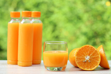 Glass of orange juice and oranges on natural green background