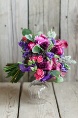 Purple bouquet with roses on a vase stand on a wooden background. Floristics and details