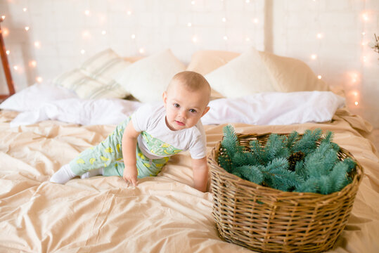 Little boy  in pajama have fun in in a Scandinavian style bedroom decorated with Christmas garlands and needles on a large bright bed. Christmas mood. Christmas mood. Family time
