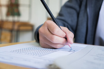 Hand Student use pencil writing on paper optical form of standardized test examination, Answer sheet,doing final exam attending in examination classroom