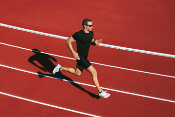 Obraz premium Mature fitness man with glasses running on the red running track. Copy space. Lifestyle and sports