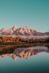 Fototapeta na wymiar Sunrise glow hits the peaks and trees of the Teton Range of the Rocky Mountains. Schwabacher Landing in Grand Teton National Park, WY, USA. Water reflections of the Teton Range on the Snake River. 