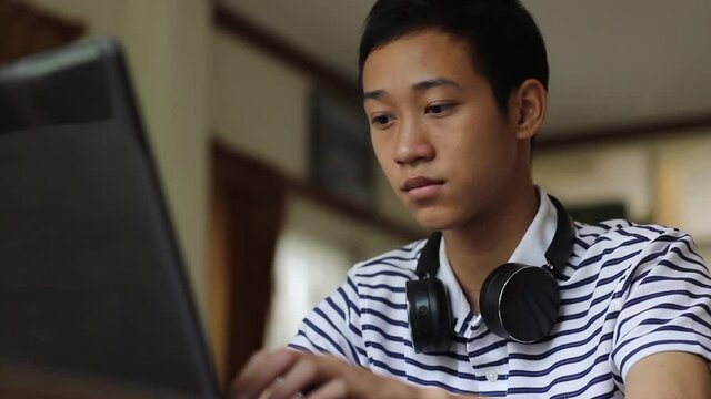 Asian boy typing laptop computer and wearing a headphone at school library. Elearning, education concept. - Powered by Adobe