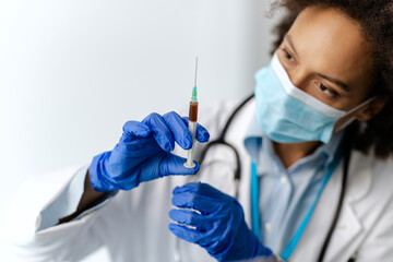 Close-up of black female epidemiologist using syringe at medical clinic.
