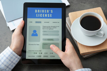 Man holding tablet with driver's license application form at grey table, closeup