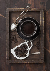 Loose black tea on cup shape ceramic plate with vintage strainer infuser in wooden box with black ceramic cup