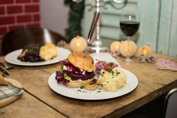 Weihnachtlicher Burger mit Rotkohl und Kartoffelpüree auf gedecktem Holztisch mit...