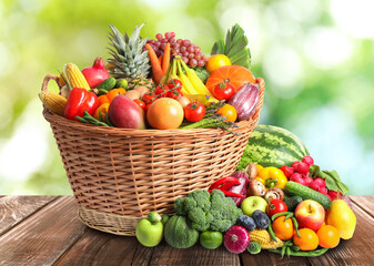 Wicker basket with different fresh organic vegetables and fruits on wooden table against blurred green background