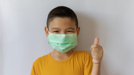 A thai boy wearing a COVID-19 anti-virus mask and dust is pretending to raise his thumb. white background in the house