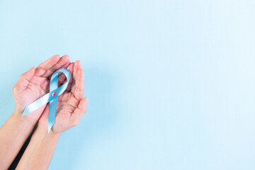 World diabetes day. Hand holding blue ribbon with blood drop inside on pastel blue background, 14 November.
