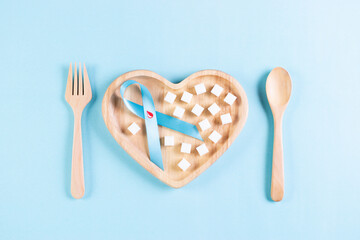 World diabetes day. Blue ribbon with blood drop inside and sugar on plate on pastel blue...