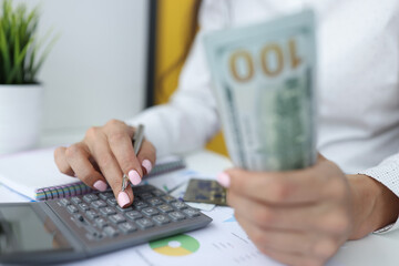 Female hands are holding one hundred dollar bills and working on calculator. Accounting in business processes concept