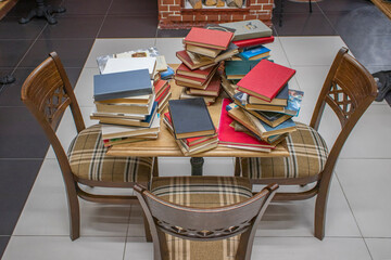 Library. Old books are stacked on the table. There are three chairs for visitors near the table.