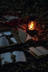 Vertical background with kerosene lamp and open books lying on the ground. Stylish Halloween background with autumn foliage and a burning kerosene lamp.