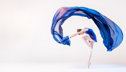 Elegant ballerina in pointes dances with developing blue cloth on white background