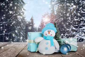 Cute toy snowman with gift boxes, decorative fir tree and Christmas balls on wooden table in winter...