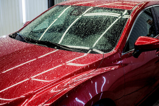 Washing red car with active foam at car wash service.