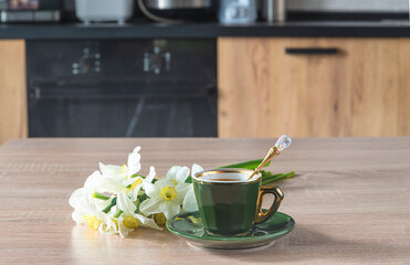 Coffee break concept. Vintage cup of coffee and bouquet of white daffodils on wooden table in the kitchen