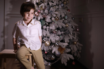 Child in smart clothes in front of the Christmas tree. Waiting for the new year.
