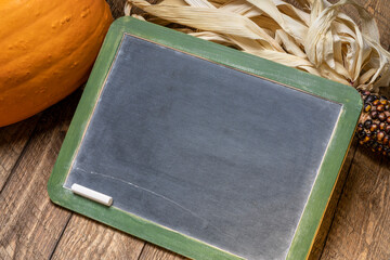 blank slate blackboard sign with pumpkin  and ornamental corn against rustic barn wood, fall holidays concept