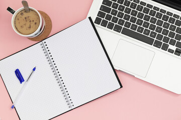 spiral notebook with laptop and white coffee on pink background