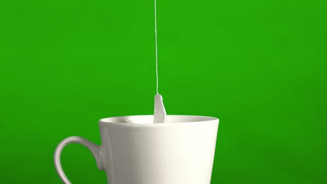 Tea bag in a white ceramic mug. Isolated on a green background. By dipping a tea bag into a white cup of hot water, after brewing, the tea bag is removed from the cup.