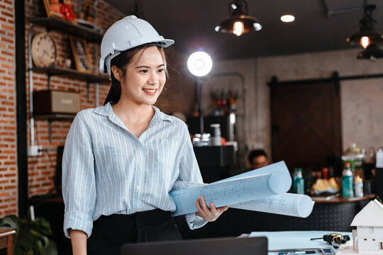 Architecture woman hold blueprints design plan and wearing safety helmet in room at site construction. Architecture, engineering, business and civil concept.