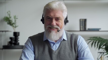 An elderly businessman in a headset having a video conference with a business partner working in an office