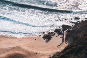 Ocean and beach view from above, shooting from above, blue waves, orange sand, rocks. Foam from...