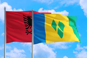 Saint Vincent And The Grenadines and Albania national flag waving in the windy deep blue sky. Diplomacy and international relations concept.