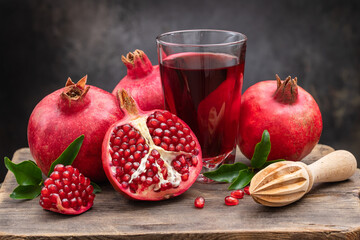 Ripe pomegranate, half a juicy pomegranate and healthy pomegranate juice in a glass on a cutting...