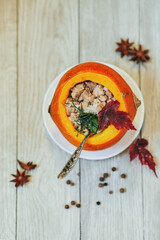 Fried chicken and porridge in pumpkin cooked with using fresh spicy herbs, hot sauce and decorative maple leaves. Hot porridge with delicious pieces of chicken. Magical fall food with natural grains