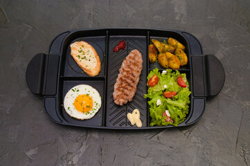 Breakfast, fried steak or cutlet, salad with tomato and green vegetables, croutons, potatoes, egg , view from the top, dark background. Concept healthy eating, diet, menu, nutritious food.