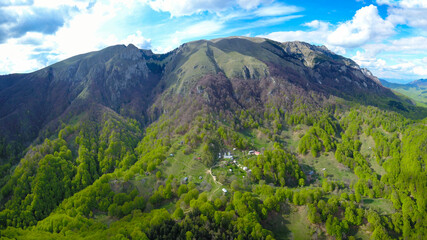 Obraz premium Aerial drone view of Buila Vanturarita Massif and Patrunsa Monastery - a rural settlement located on the hills at the base of the mountain.