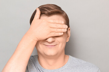 Portrait of happy optimistic mature man covering eyes with one hand