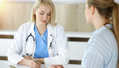 Woman-doctor and patient sitting and talking in sunny clinic. Blonde therapist is cheerfully smiling