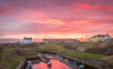 The Burn with the moored fishing boats of Seaton Sluice, Northumberland at sunrise, with the fiery...