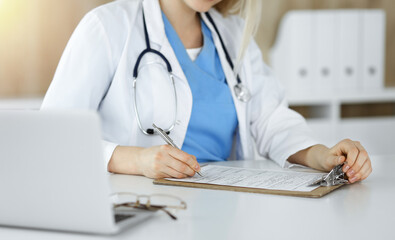 Unknown woman-doctor at work filling up medication history record form in sunny clinic, close-up