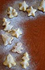Line of christmas cookies shaped like a gingerbread man, bells, christmas trees and stars on a wooden background with powdered sugar sprinkled