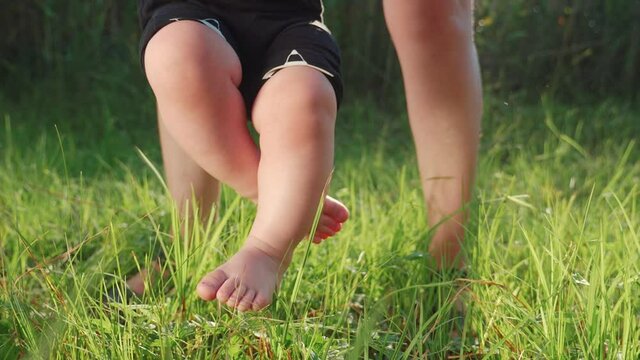 baby does first steps grass happy family. mom helps baby son take steps with his feet. people in the park dream kid concept happy family childhood lifestyle. child son walks barefoot on green grass