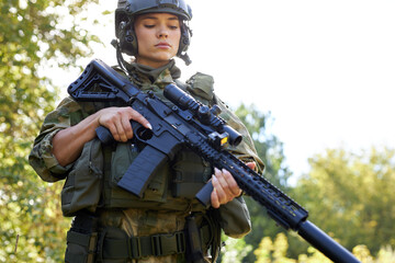 young caucasian military woman is checking rifle in the forest before shooting, alone in nature, female soldier